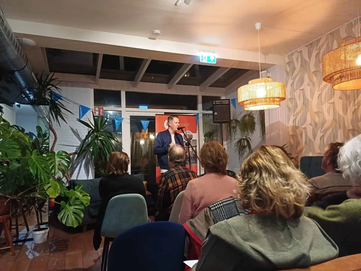 Timon Kitsz spreekt voor een aandachtig publiek tijdens een bijeenkomst in een sfeervol ingerichte zaal.